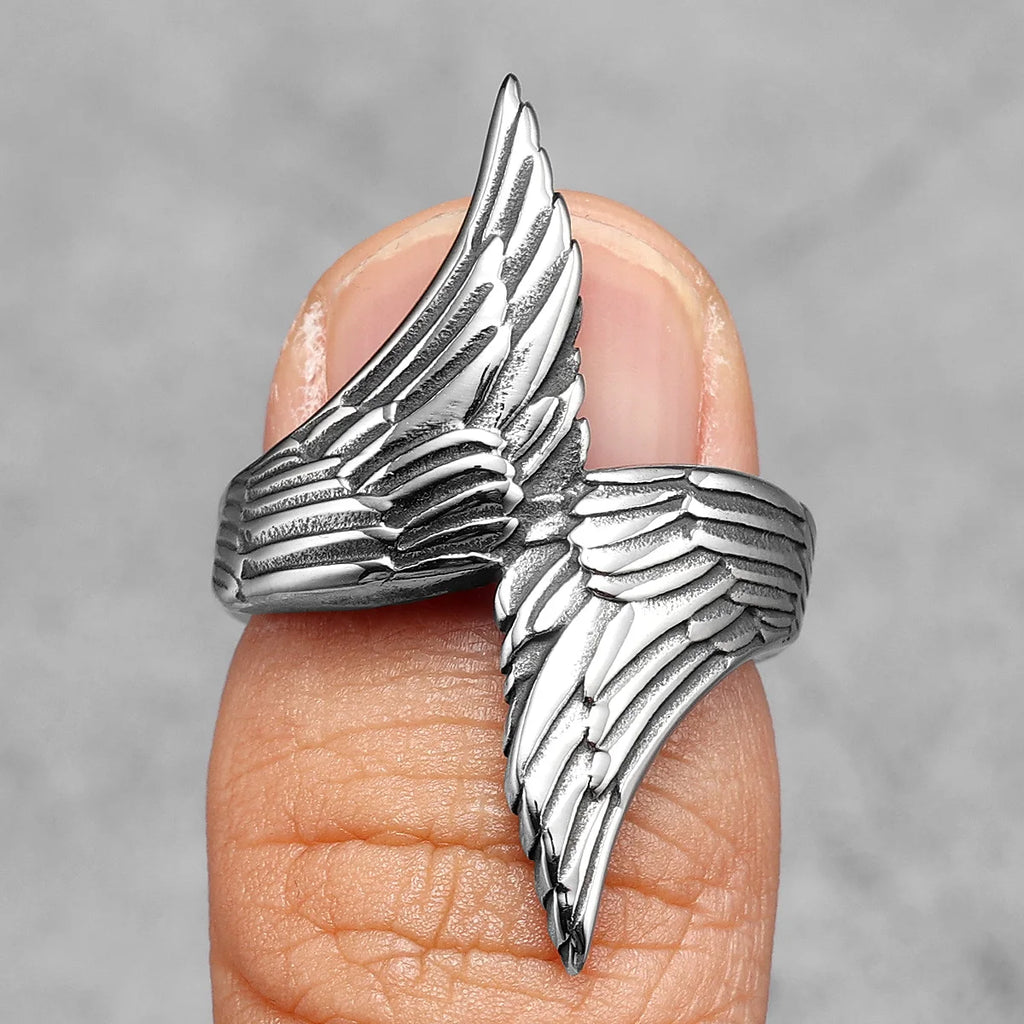 Silver angel bird wing-shaped ring on a finger against a grey background