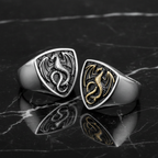 Two dragon-themed rings, one silver and one gold, on a dark marble surface.