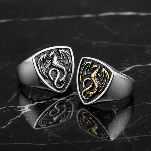 Two dragon-themed rings, one silver and one gold, on a dark marble surface.