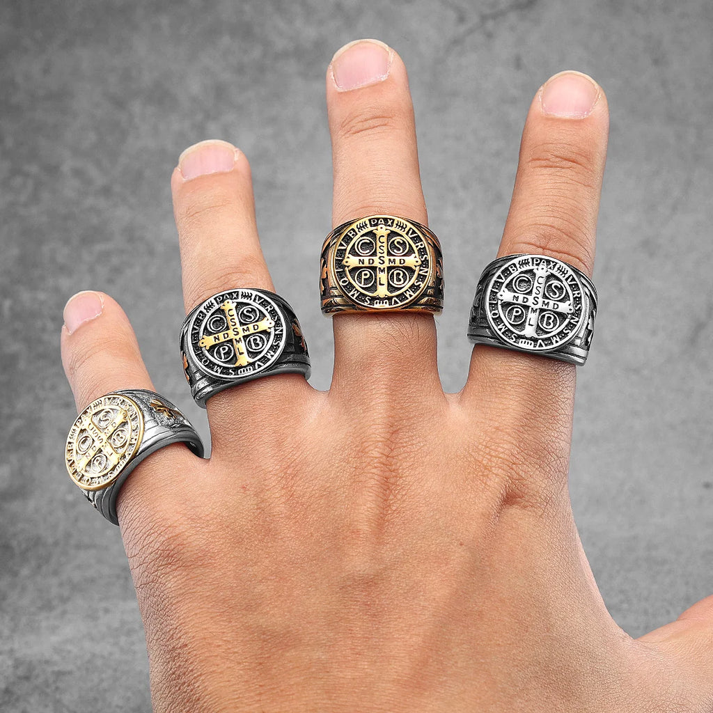 Hand wearing four decorative rings with intricate designs on a grey background