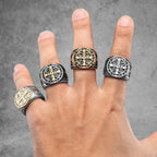 Hand wearing four decorative rings with intricate designs on a grey background