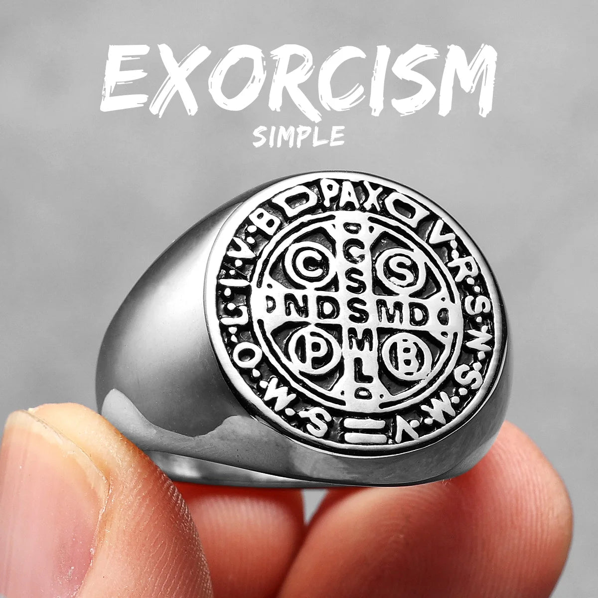 Silver ring with intricate designs held by a hand against a grey background, featuring the word 'Exorcism'.