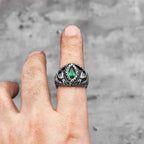 Silver fantasy snake scale ring with a green gemstone on a finger against a grey background