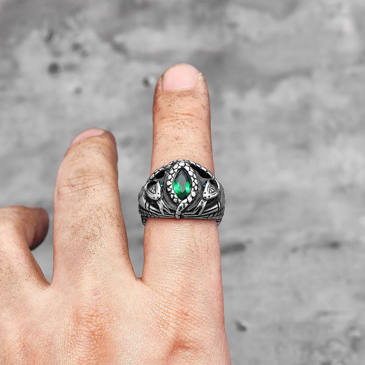 Silver fantasy snake scale ring with a green gemstone on a finger against a grey background