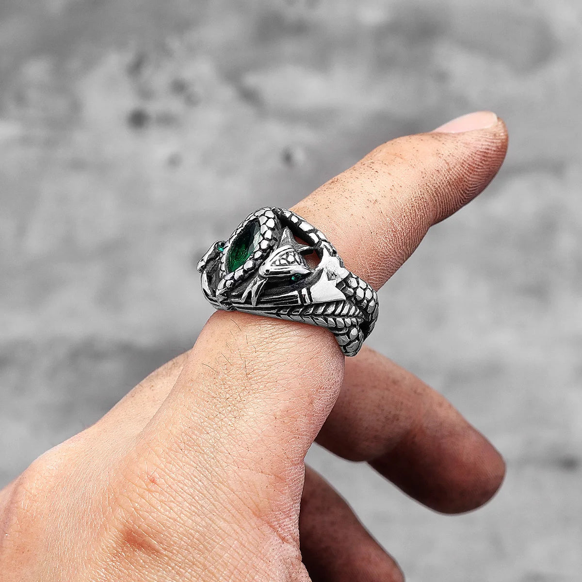 Silver ring with green gemstone on a finger against a blurred background
