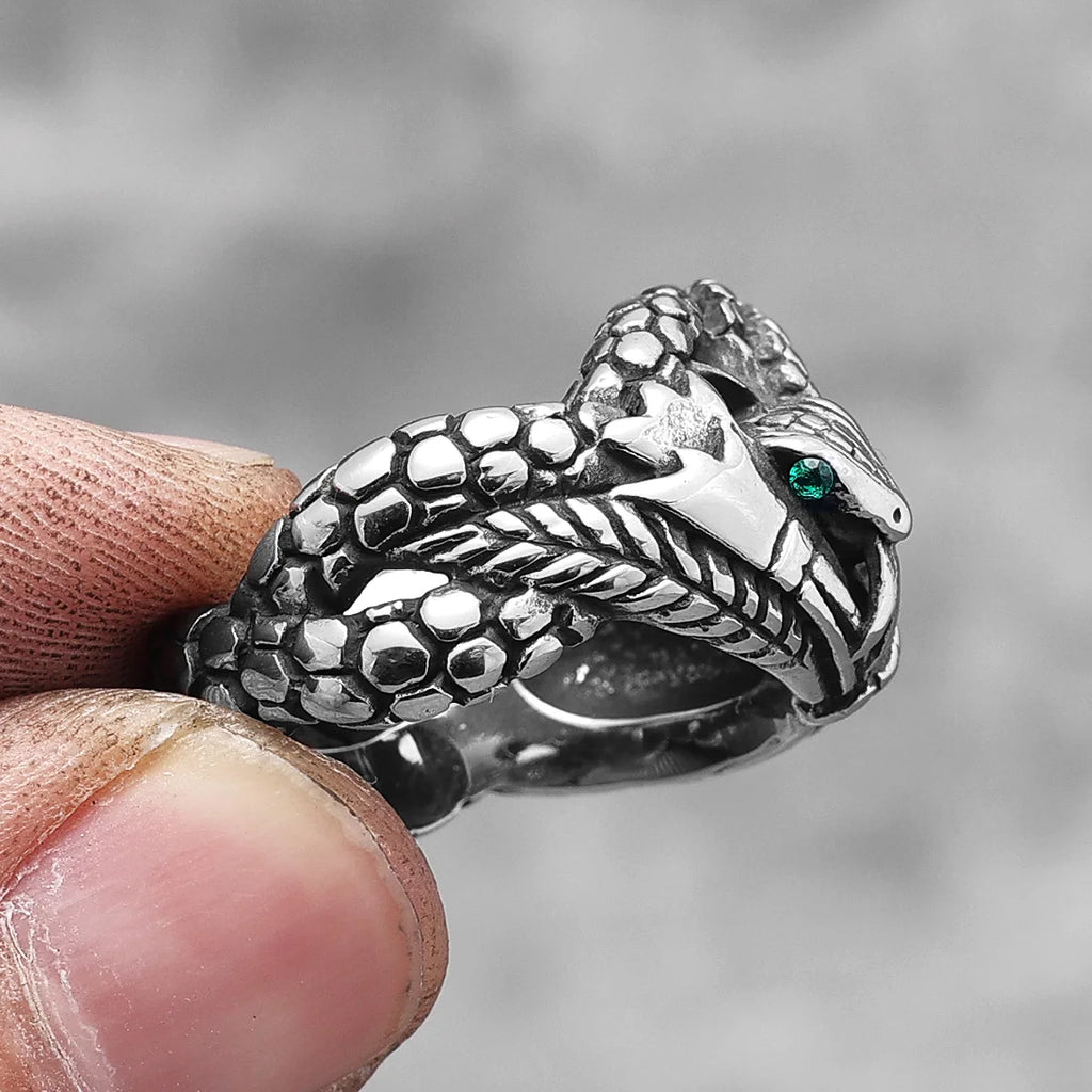 Silver snake-shaped ring with a green stone held between fingers against a blurred background