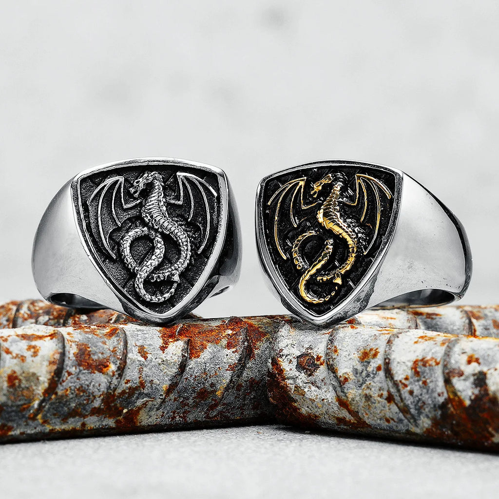 Two dragon-themed rings on a rustic metal surface with a grey background