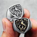 Two dragon-themed rings held in a hand against a grey background