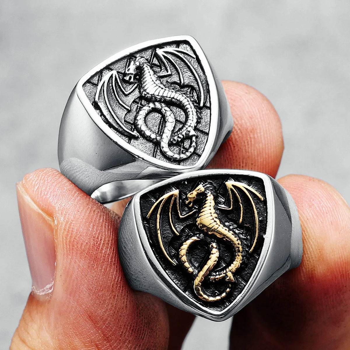 Two dragon-themed rings held in a hand against a grey background