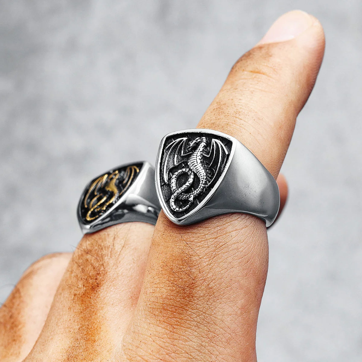Silver ring with dragon design worn on a finger against a grey background