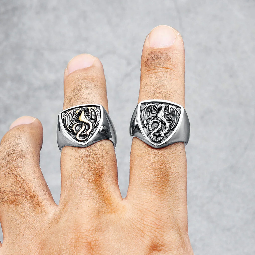 Two silver dragon-themed rings on a person's fingers against a grey background