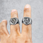 Two silver dragon-themed rings on a person's fingers against a grey background