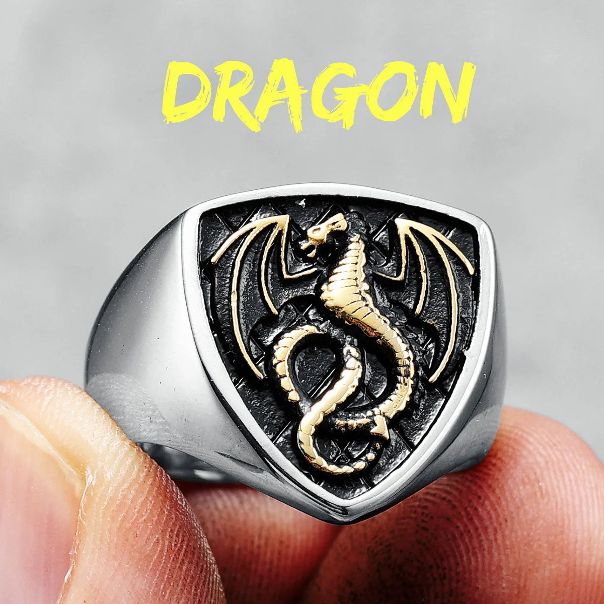 Gold ring with dragon design held between fingers against a grey background