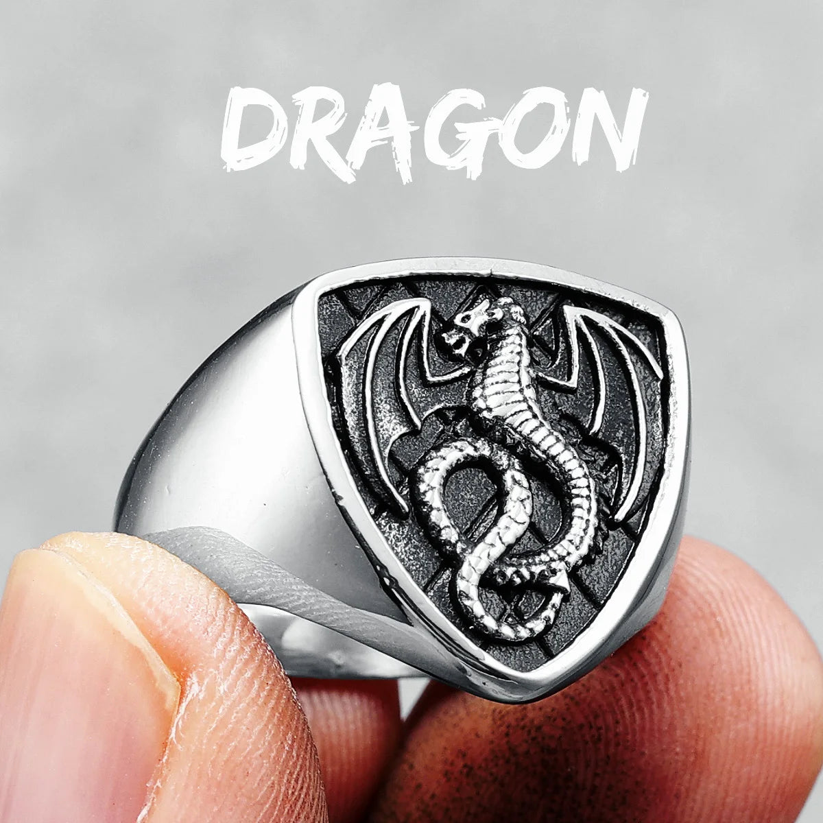 Silver dragon ring held between fingers with 'DRAGON' text above on a grey background