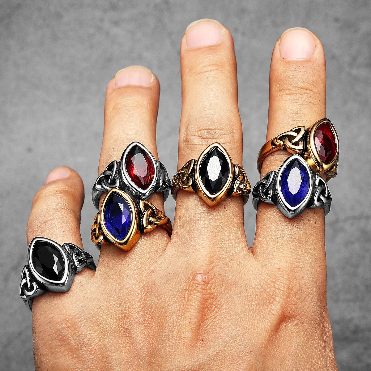 Four ornate rings with gemstones on a finger against a grey background