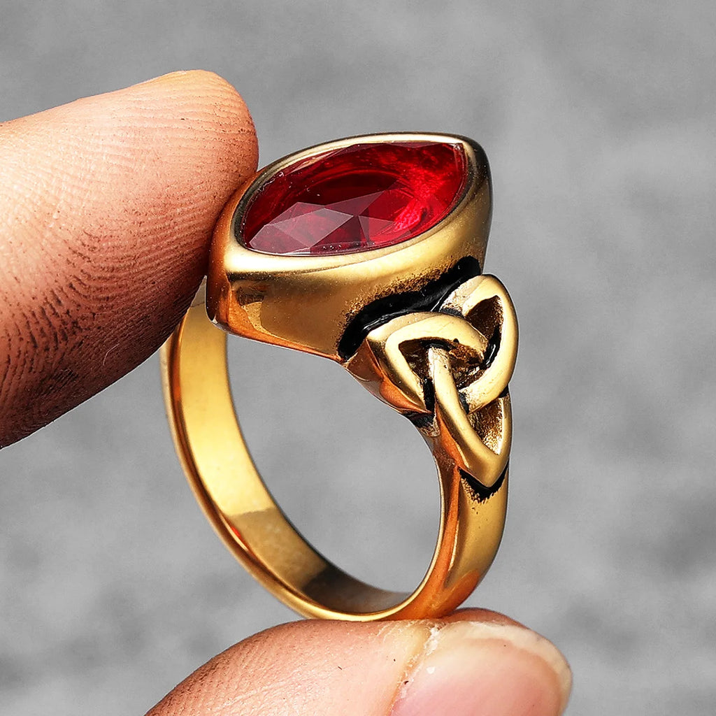 Gold ring with a red gemstone held between fingers against a grey background