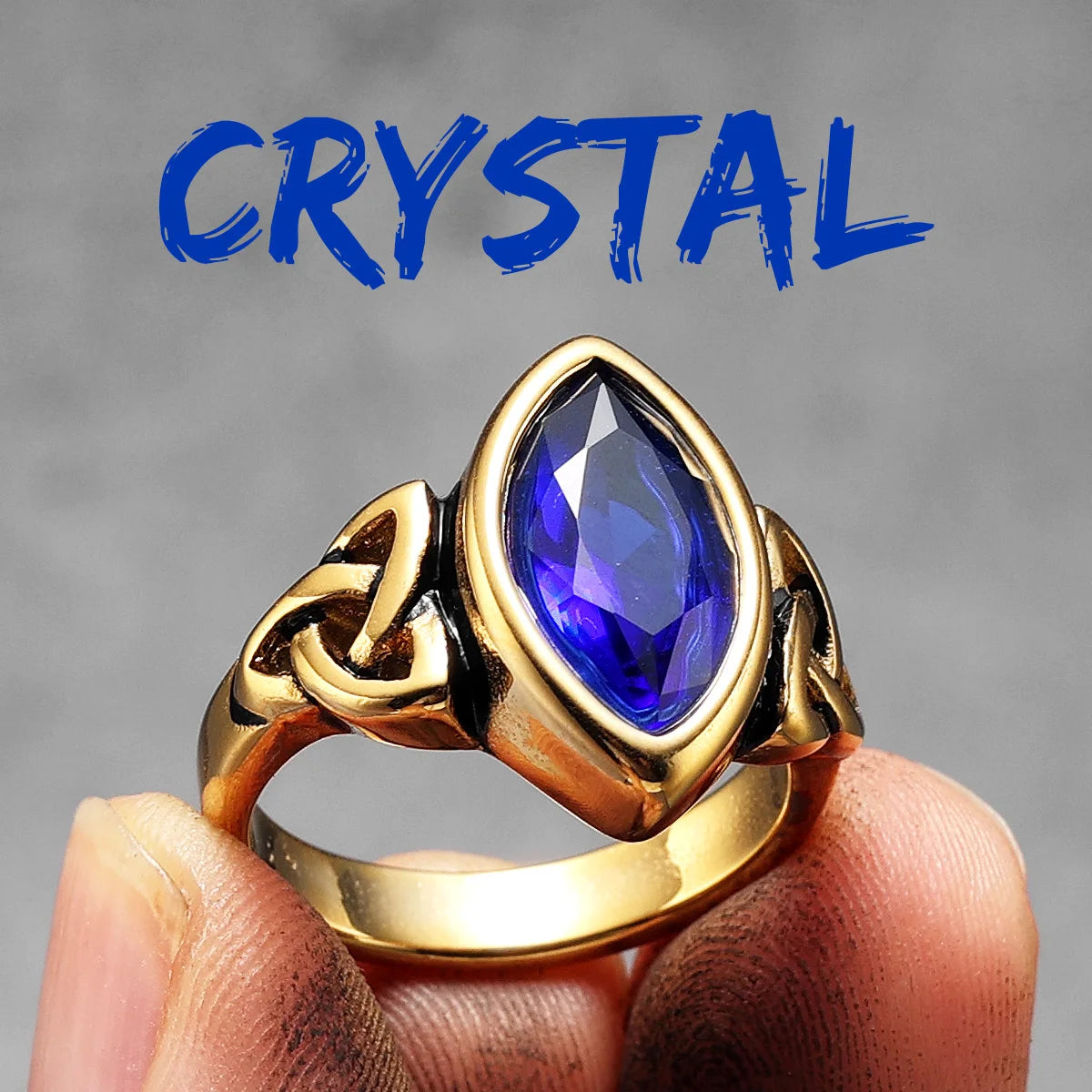 Gold ring with a blue gemstone held on a finger against a grey background