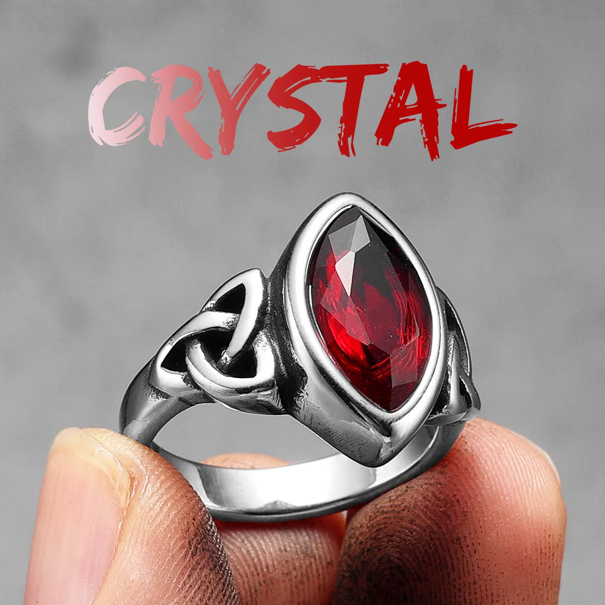Silver elven ring with a red gemstone held by a hand against a grey background 