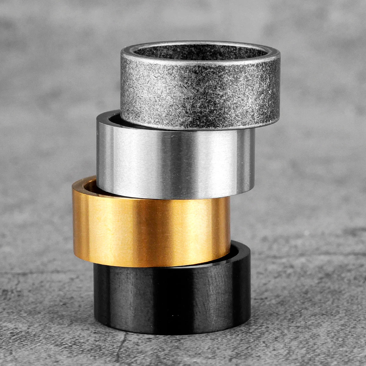 Stack of metal rings in silver, gold, and black on a textured grey surface