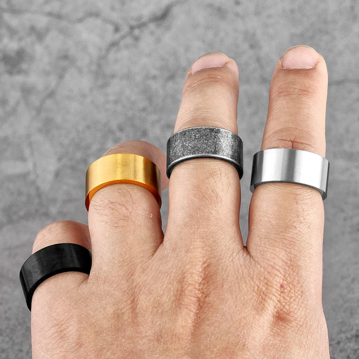 Hand wearing five different rings on a grey background
