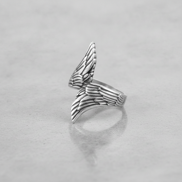 Silver wing-shaped ring on a light grey background