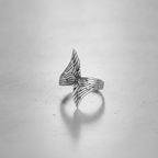 Silver wing-shaped ring on a light grey background