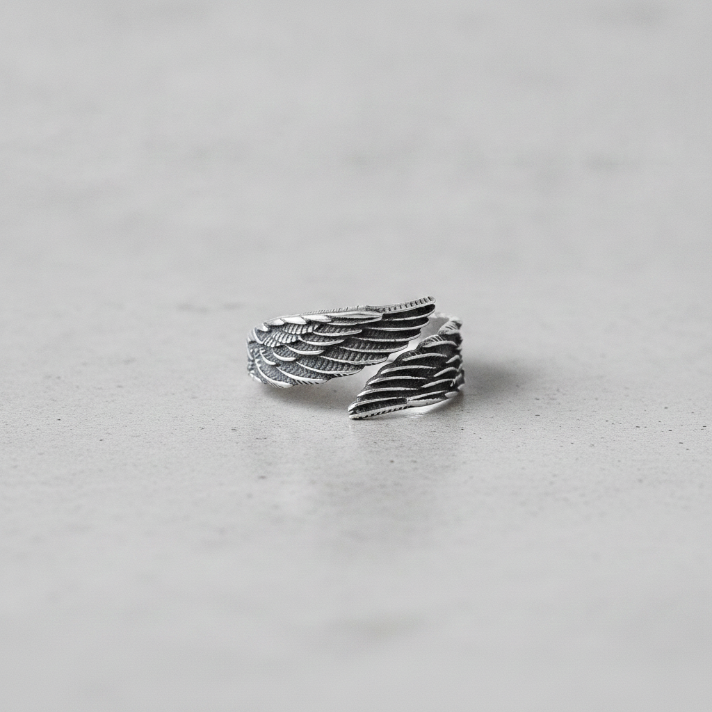 Silver wing-shaped ring on a light grey background