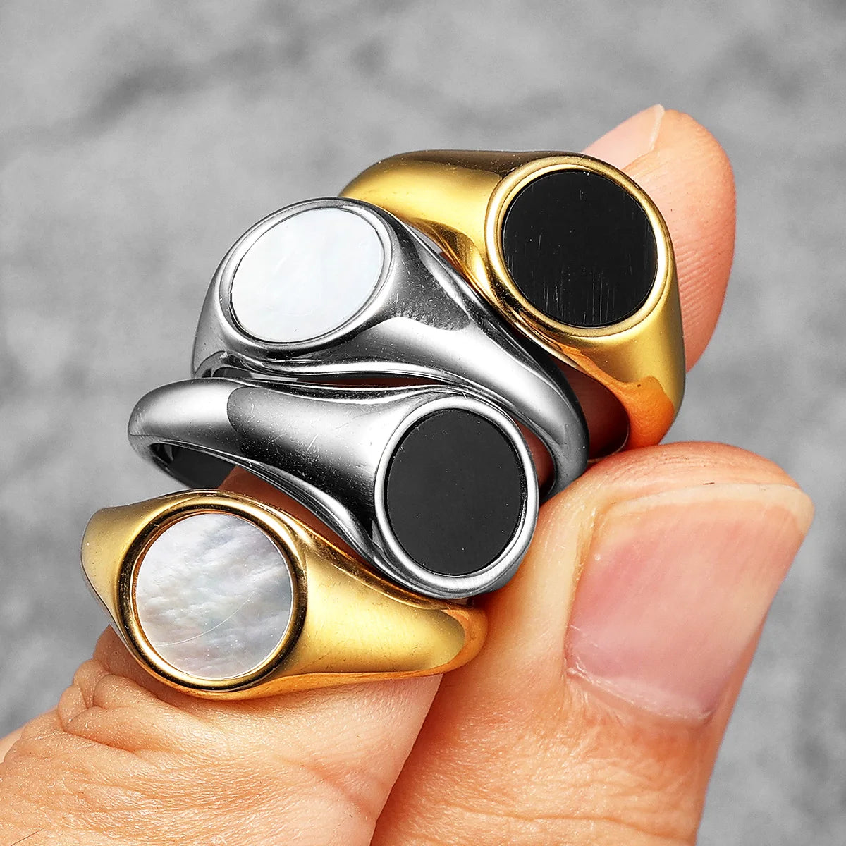 Four metallic rings with different coloured stones on a finger against a grey background