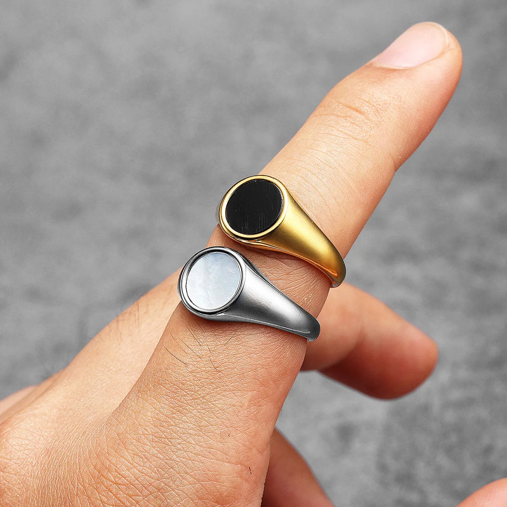 Two pearl rings, one gold and one silver, on a finger against a grey background