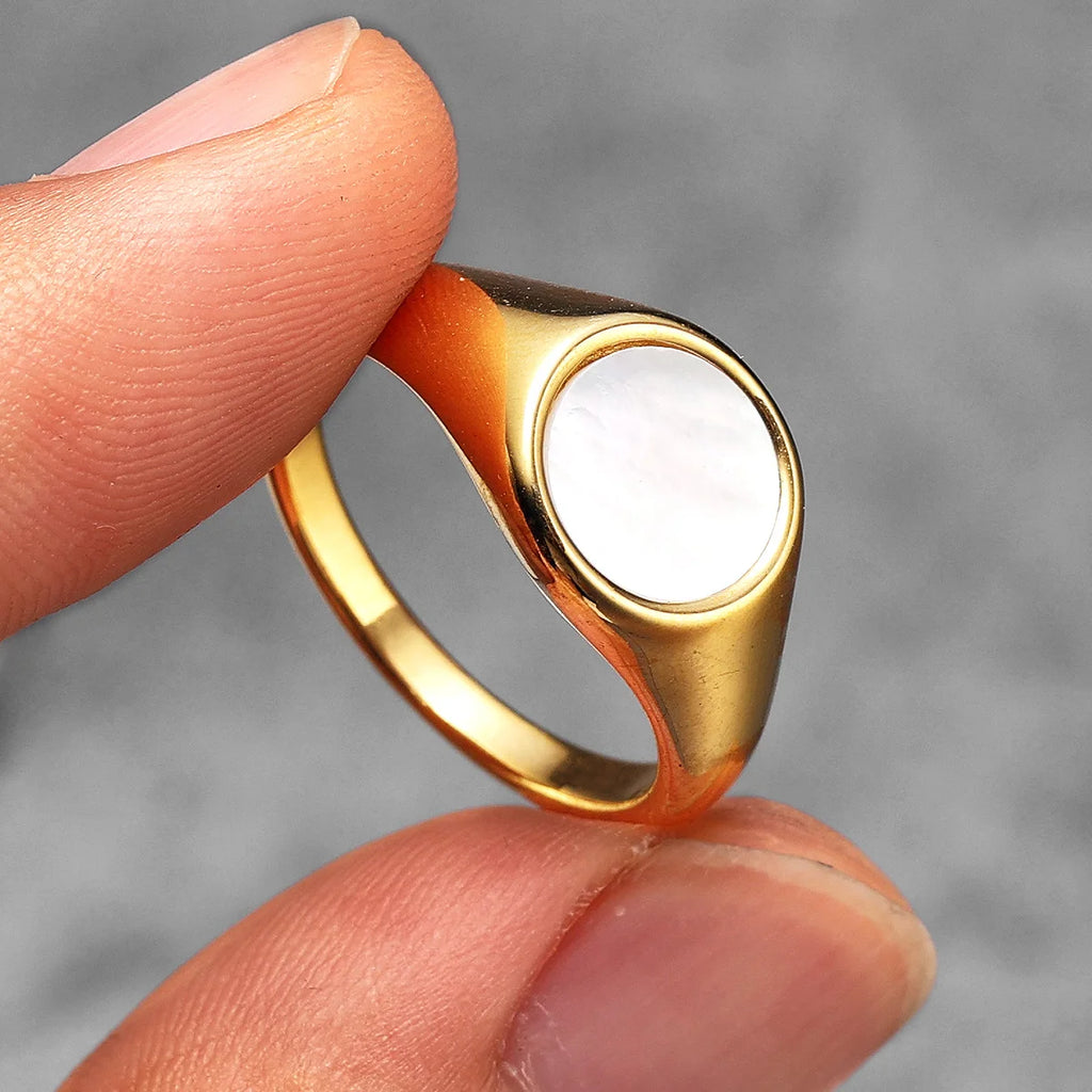 Gold ring with a white stone held between fingers against a gray background