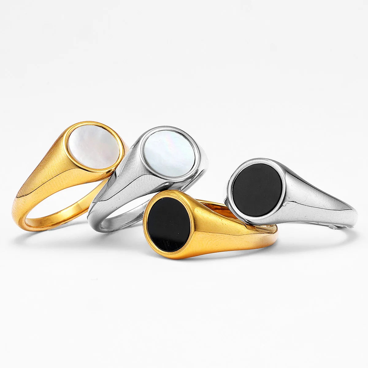 Four pearl and shell signet rings in gold and silver with black and white stones on a light grey background
