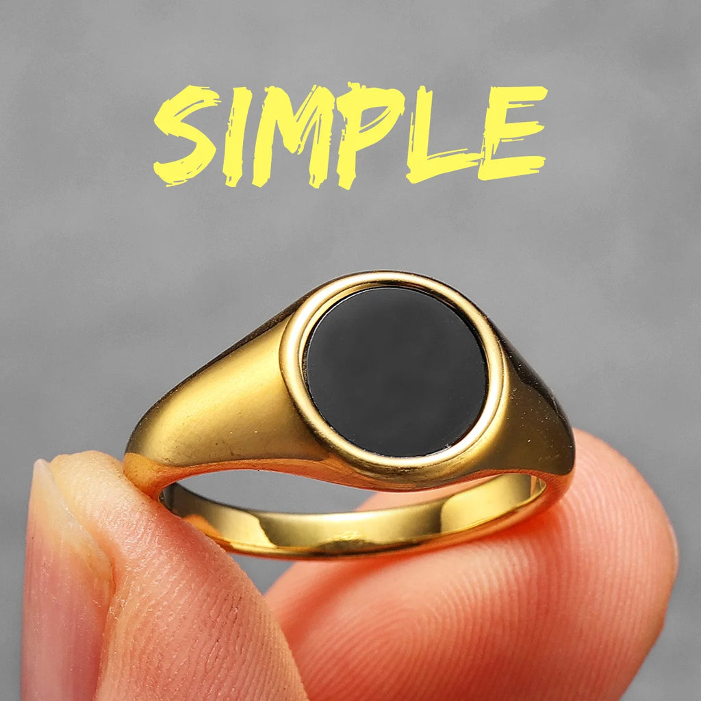 Gold ring with a black centre held by a hand against a grey background with the word 'SIMPLE' in yellow.
