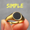 Gold ring with a black centre held by a hand against a grey background with the word 'SIMPLE' in yellow.