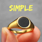 Gold ring with a black centre held by a hand against a grey background with the word 'SIMPLE' in yellow.