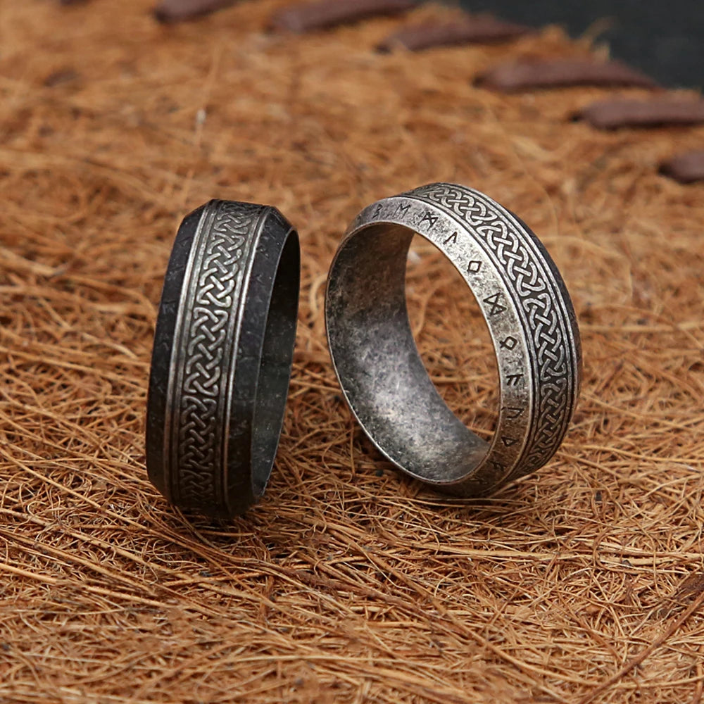 Two silver rings with intricate viking rune designs on a textured brown surface