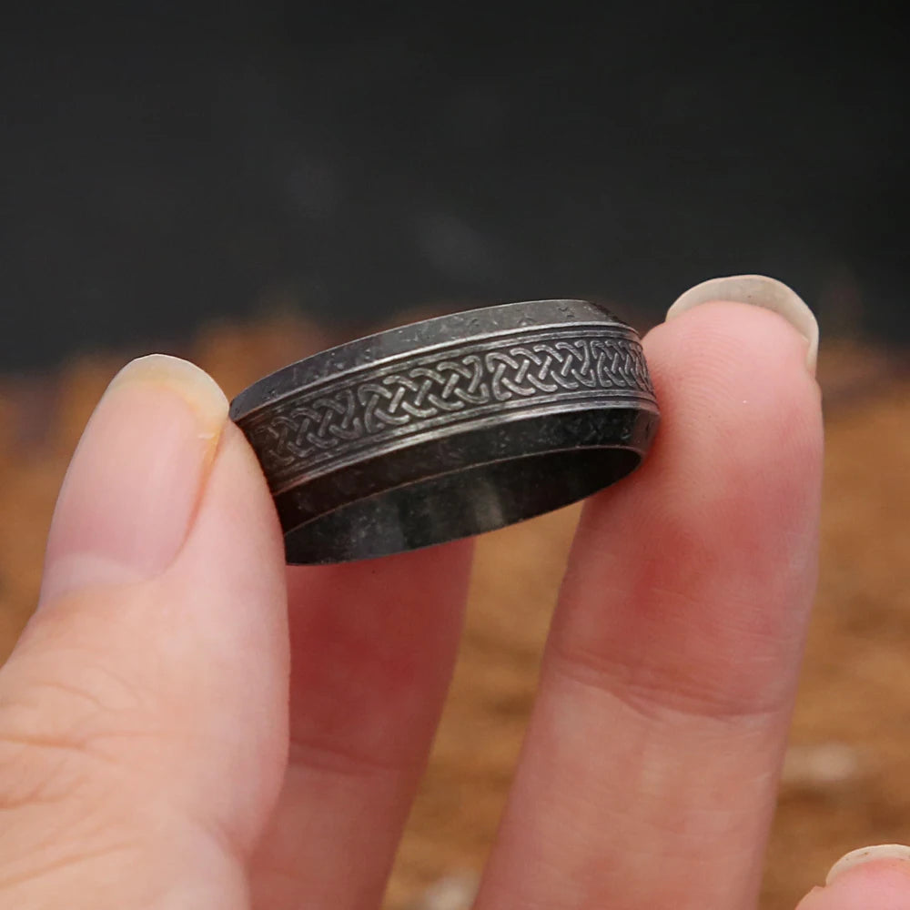 Dark Grey ring with intricate Nordic design held between fingers against a blurred background