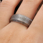 Light grey ring with Celtic knot design and engraved text on a person's finger.