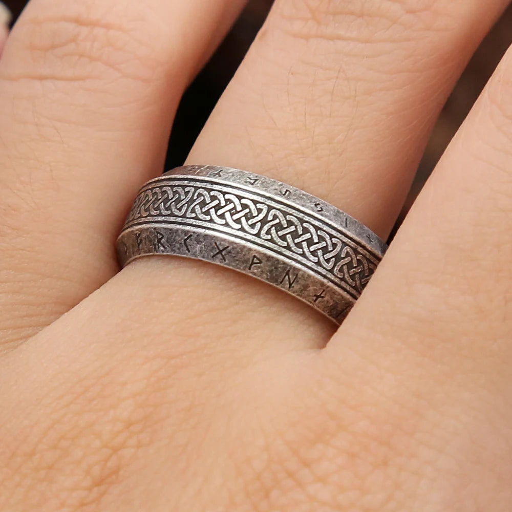 Light grey ring with Celtic knot design and engraved text on a person's finger.