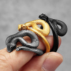 Three snake-shaped rings in gold, silver, and black on a finger against a grey background