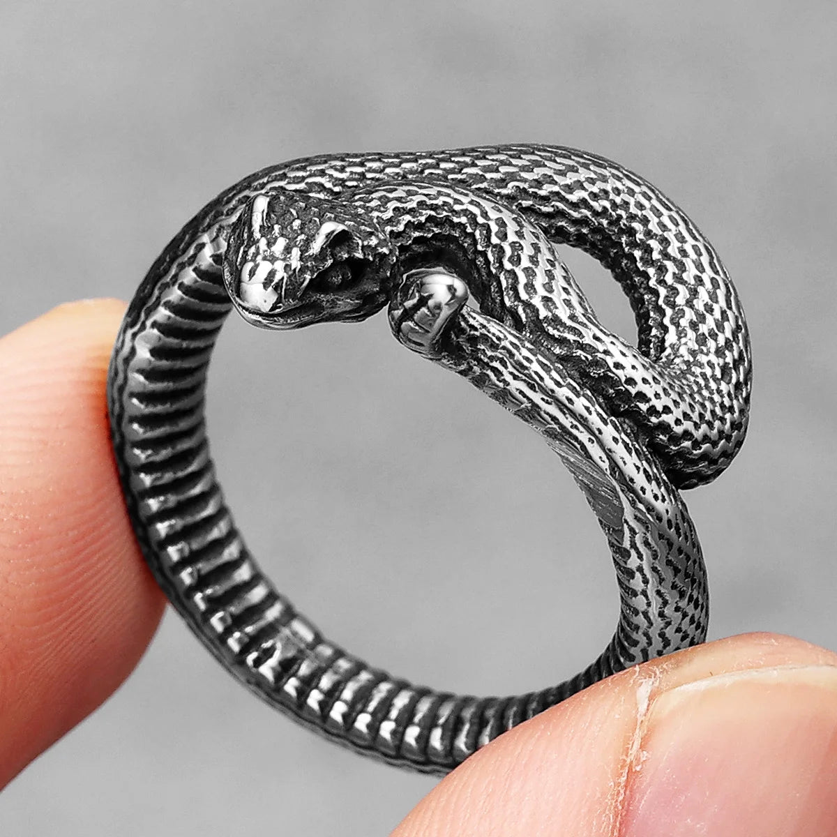 Silver snake-shaped ring on a finger against a grey background