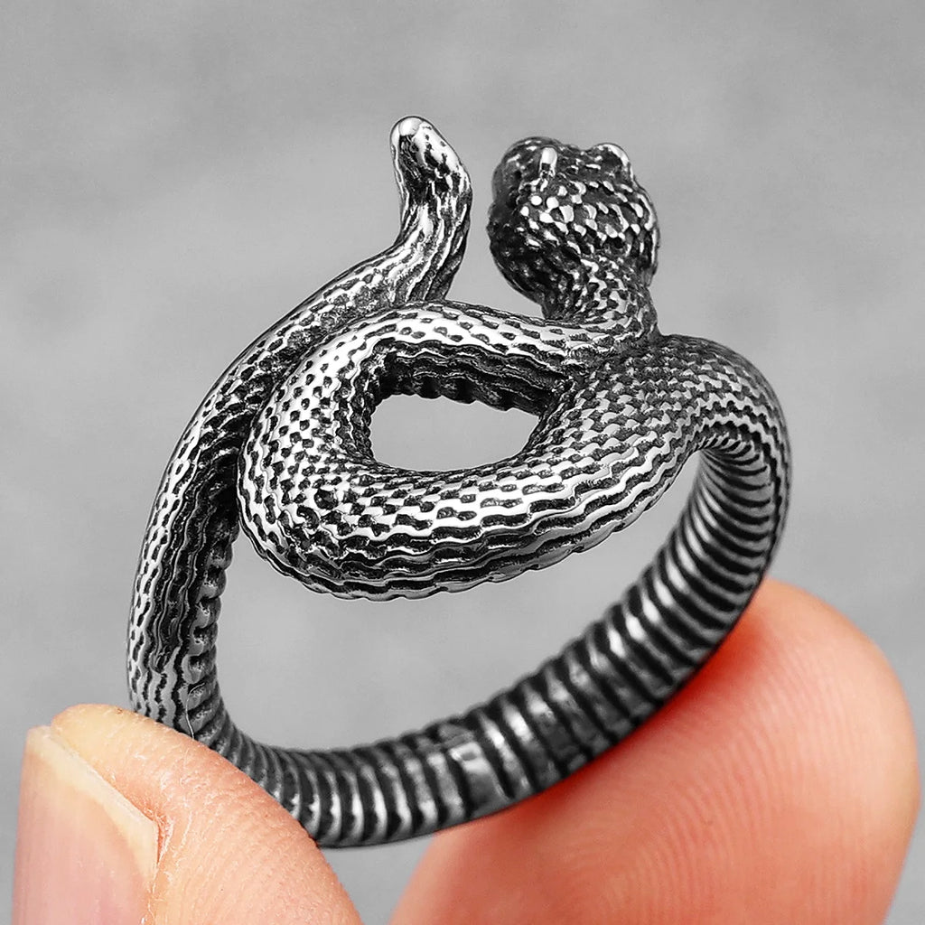 Silver snake-shaped ring held between fingers against a grey background
