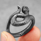 Silver snake-shaped ring held between fingers against a grey background
