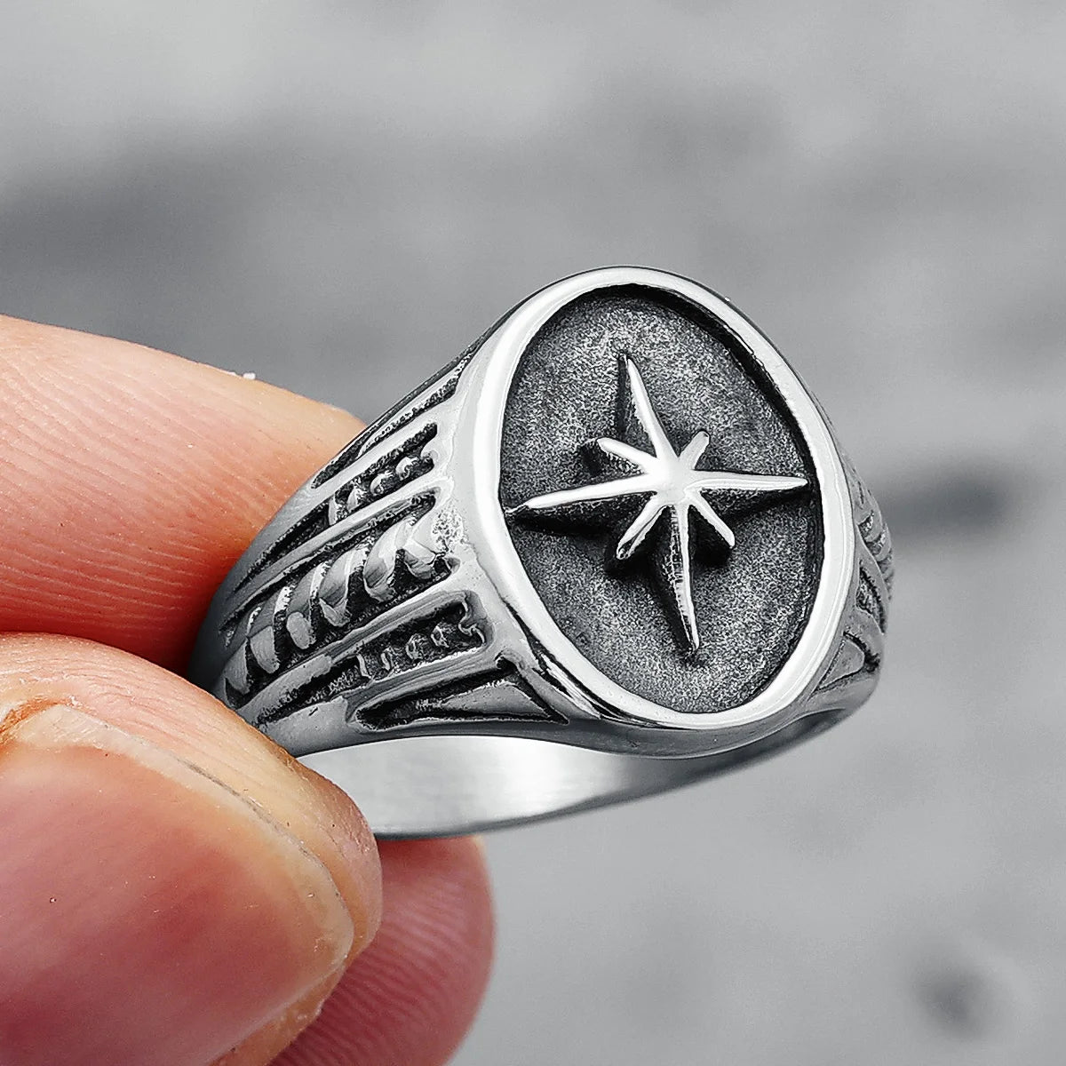 Silver ring with star design held by a hand against a blurred background