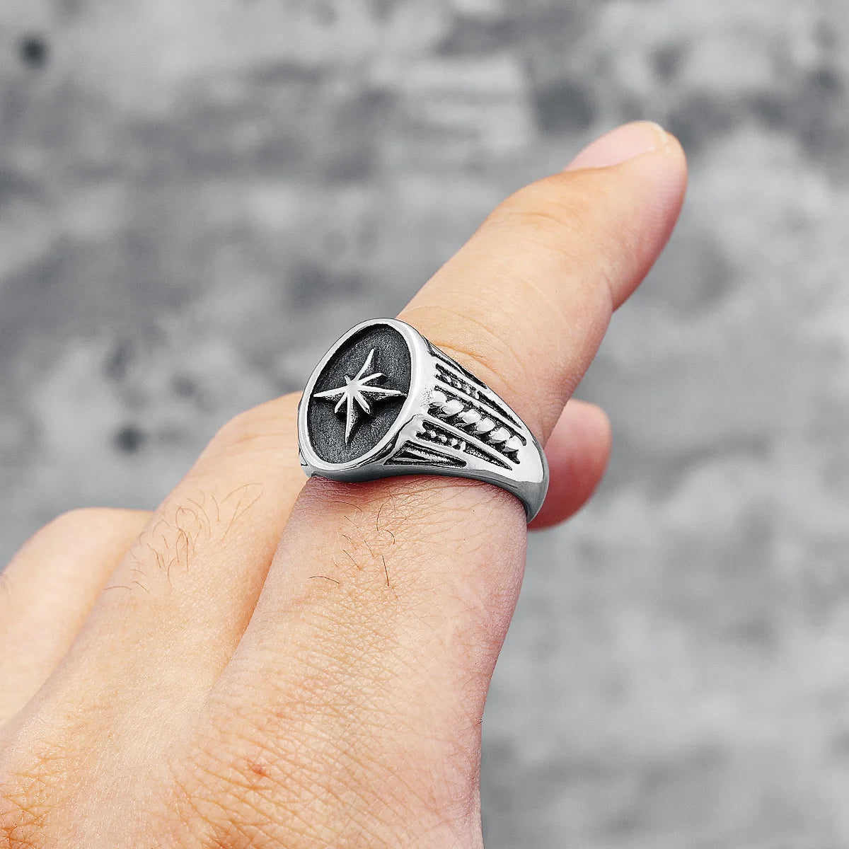 Silver ring with star design worn on a finger against a blurred grey background