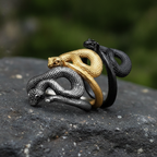 Three snake-shaped rings in gold, silver, and black on a dark surface with a blurred green background.