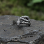 Silver snake-shaped ring on a dark stone surface with a blurred green background