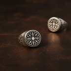Two silver rings with compass designs on a brown leather background