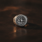 Silver ring with compass design on a dark brown leather surface