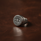 Silver ring with intricate design on a brown leather background