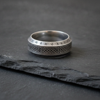 Silver ring with engraved Viking rune patterns on a dark charcoal stone surface